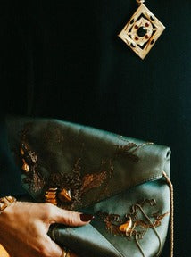 The Hathor Spinning Pendant Necklace in black onyx worn over a dark green dress, with a hand holding an embroidered clutch