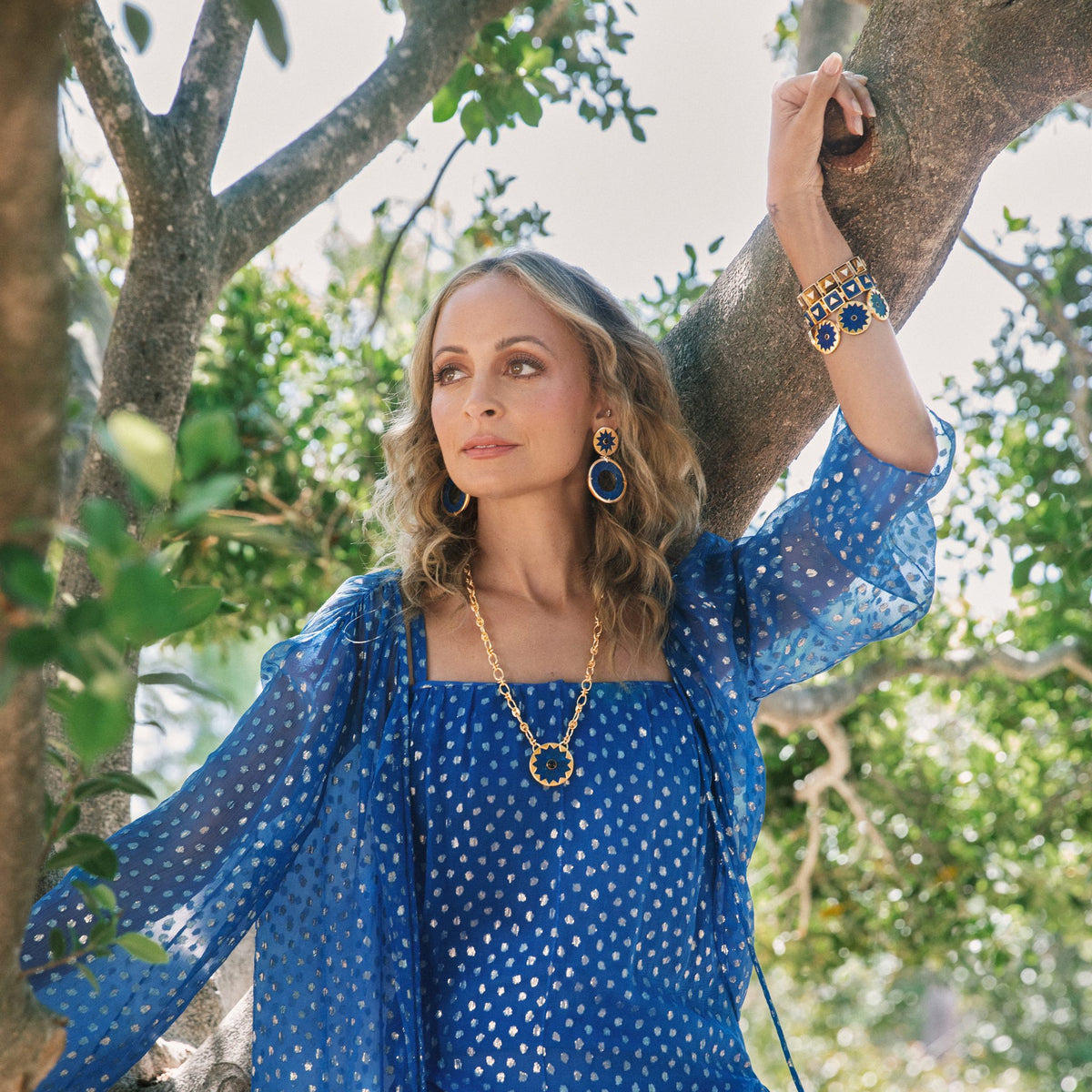 Nicole Richie in a blue dress in a tree wearing the Sunburst Pendant Necklace and Statement Earrings in blue lapis