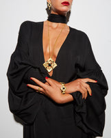 Model wearing the Hathor Spinning Pendant Necklace long over a black draped dress, with a gold cuff bracelet and rings